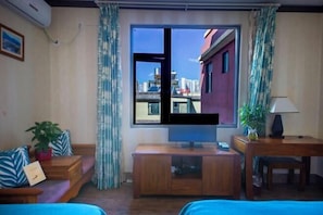 A room with a large window, a television, a sofa, a small table, and a desk. - Boao Yingke Hotel (Dali City)