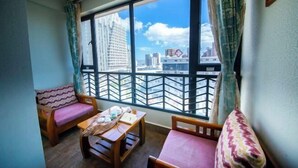 A balcony with a view of city buildings, a wooden table with a cushion, and two wooden chairs. - Boao Yingke Hotel (Dali City)