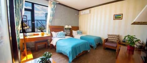 A hotel room with two beds, a desk, a chair, and a view of the outside.