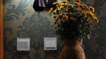 A room with a patterned wallpaper, a vase with yellow flowers, and two wall-mounted light switches.