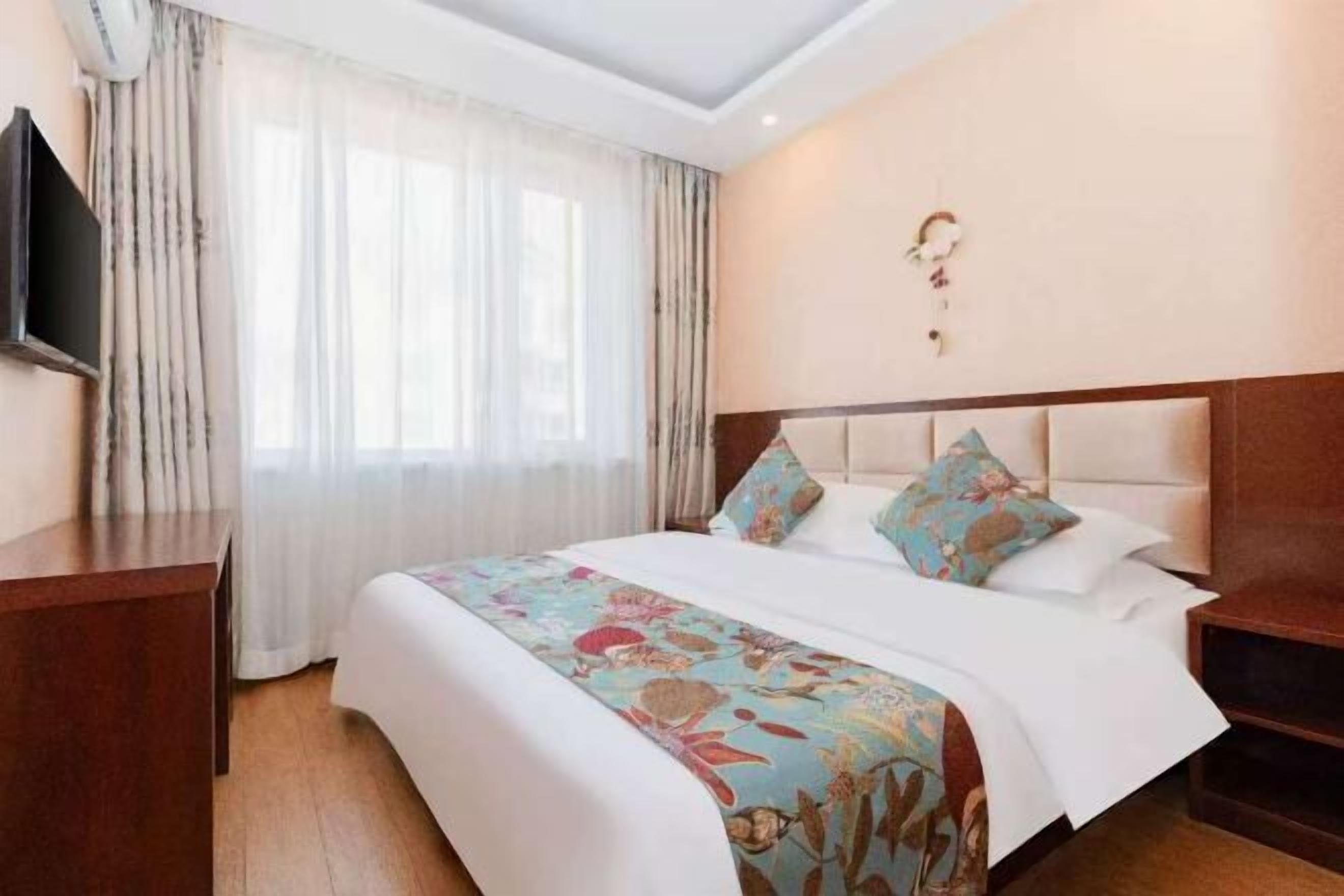 A hotel room with a bed, a TV, a desk, and a window with curtains.