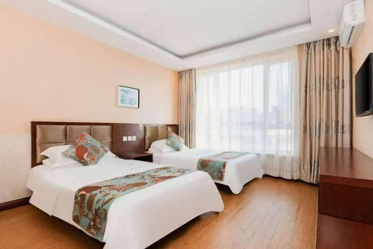 A hotel room with two beds, a large window with curtains, a flat-screen TV, and a wooden floor.