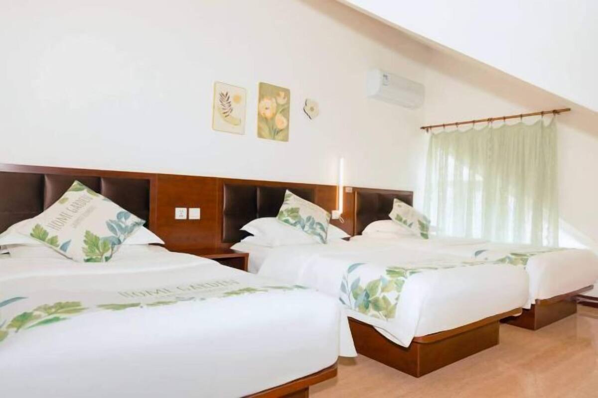 A hotel room with two beds, a wooden headboard, a small bedside table, and a window with a sheer curtain.