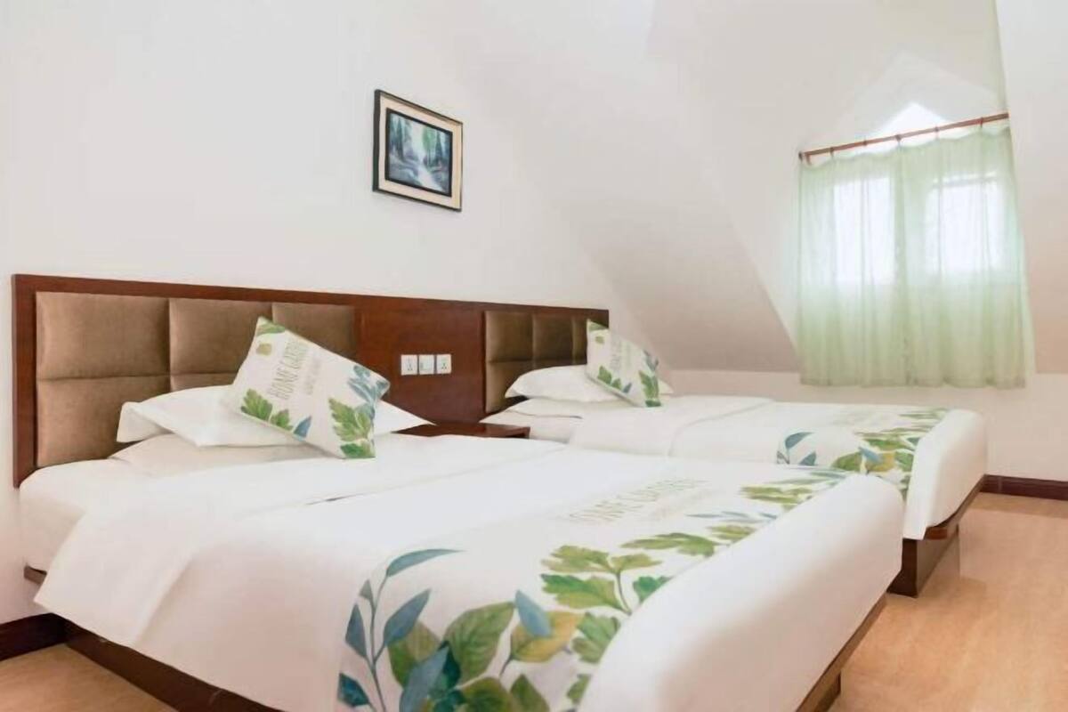 A hotel room with two beds, a framed picture on the wall, and a window with a sheer curtain.