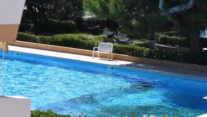 En swimmingpool med kristallklart blått vatten, omgiven av grönska och en vit stol.