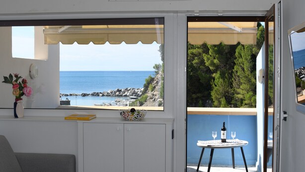 En balkong med utsikt över havet, ett bord med vinglas och en vas med blommor.