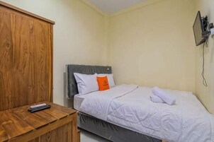 A single bed with a grey headboard, a wooden nightstand, and a wall-mounted phone.
