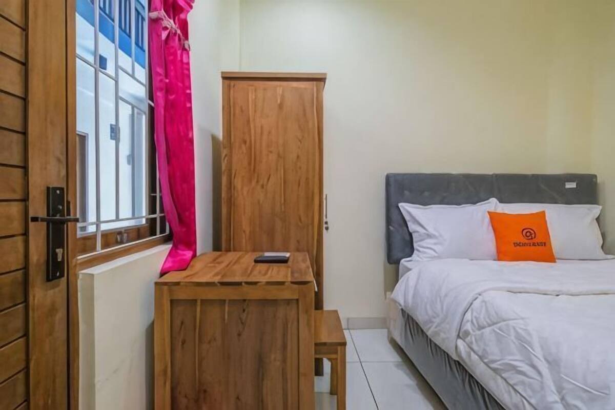 Um quarto com uma cama, um armário de madeira, uma mesinha e uma janela com cortinas.