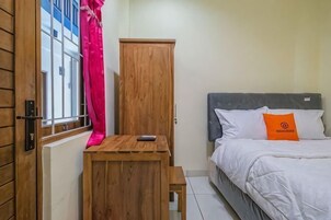 A bedroom with a bed, a wooden cabinet, a small table, and a window with curtains.