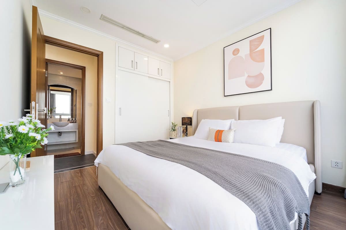 A hotel room with a large bed, a bedside table, a nightstand, a mirror, a wardrobe, and a bathroom visible through an open door.