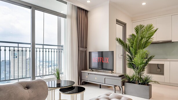 A modern living room with a sofa, a TV, a dining table, and a kitchen area. - Vinhomes Central Park - The Landmark (Ho Chi Minh City)