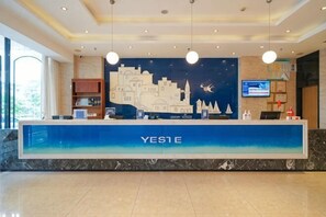 A reception desk with 'YES1E' signage, a cityscape mural, a television screen, and a marble floor. - Yeste Hotel (Nanning Jiuquwan Hot Spring) (Nanning)