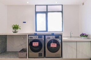 A laundry room with two washing machines, a sink, and a window above. - Yeste Hotel (Nanning Jiuquwan Hot Spring) (Nanning)