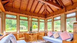 A cozy room with a wooden ceiling, large windows, a sofa, a table, and chairs.