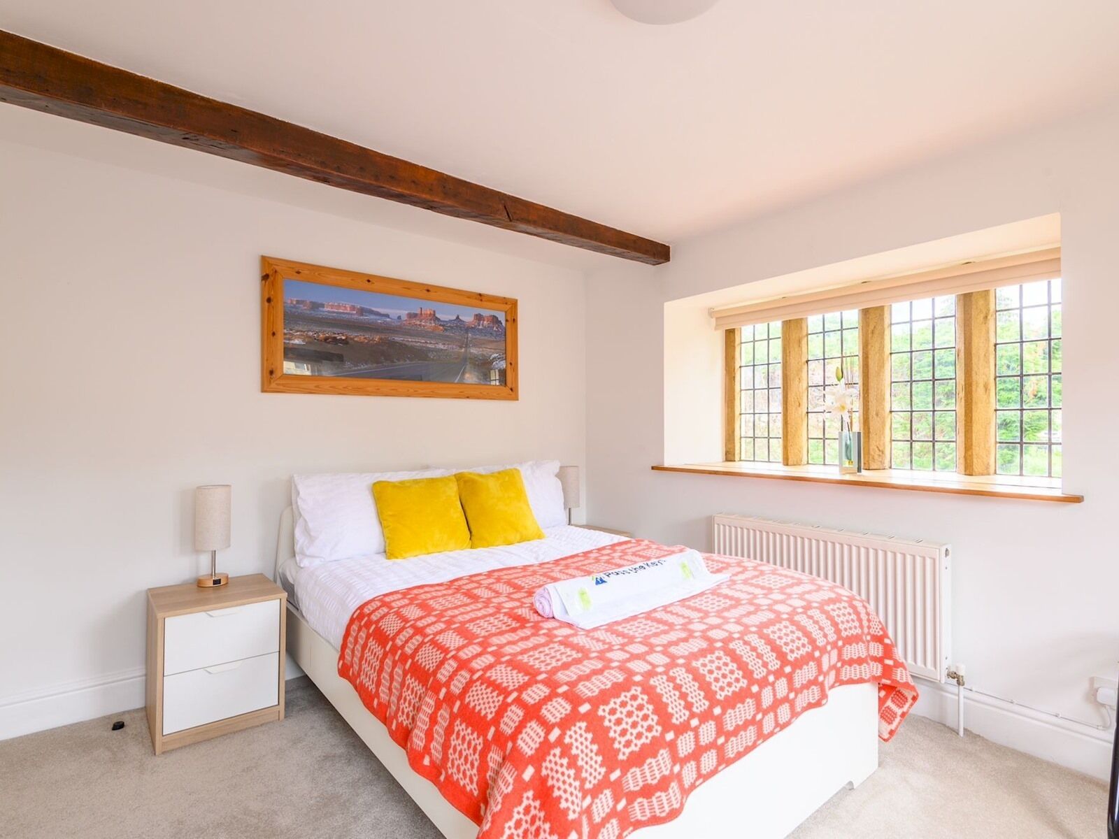 A bedroom with a bed, a nightstand, a window, and a painting on the wall.