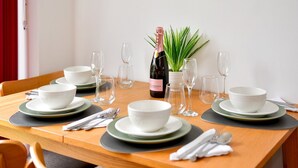 Una mesa de comedor dispuesta con cuencos, platos y cubiertos blancos, una botella de champán y una planta en maceta.