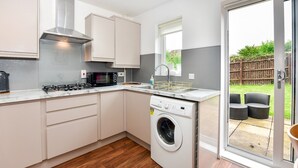 Una cocina moderna con armarios blancos, microondas integrado, cocina a gas y lavadora.