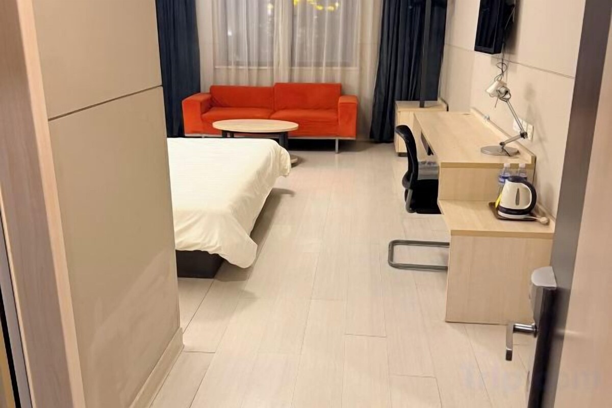 Habitación de hotel pequeña y funcional con cama, una mesita redonda, sofá y zona de kitchenette.