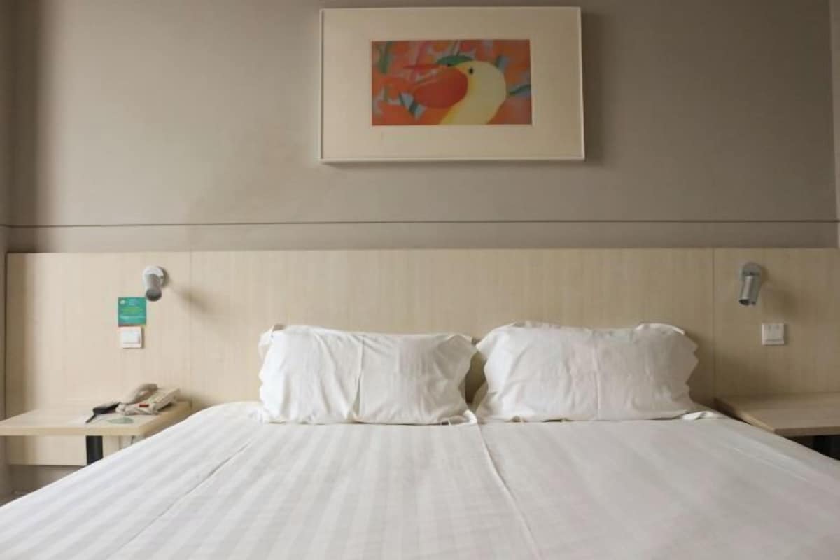 A hotel room with a bed, two pillows, a bedside table with a phone, and a framed picture on the wall.