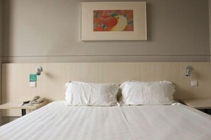 Habitación de hotel con cama, dos almohadas, mesita de noche con teléfono y un cuadro enmarcado en la pared.