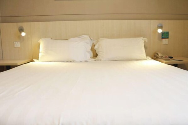 Una habitación de hotel con una cama grande, dos lámparas de noche y una mesita de noche con teléfono.