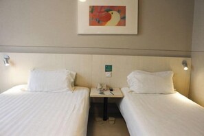 Habitación de hotel con dos camas individuales, una mesita con un teléfono y una lámpara, y un cuadro en la pared.