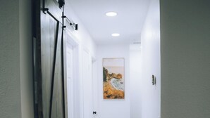 Un couloir étroit doté d’un parquet en bois foncé, de murs blancs et d’une porte avec une poignée noire.