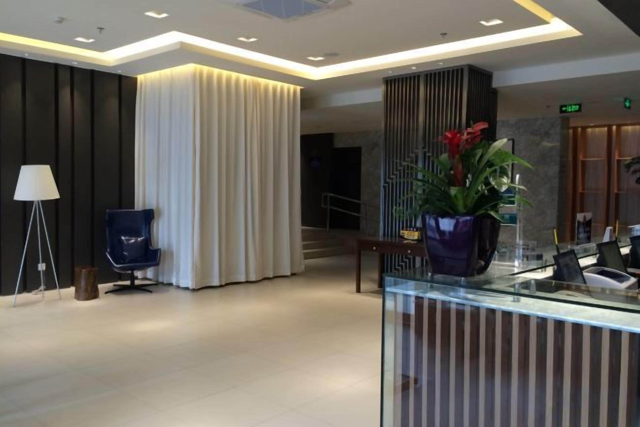 A modern hotel lobby with a reception desk, a blue chair, a large curtain, and a staircase.