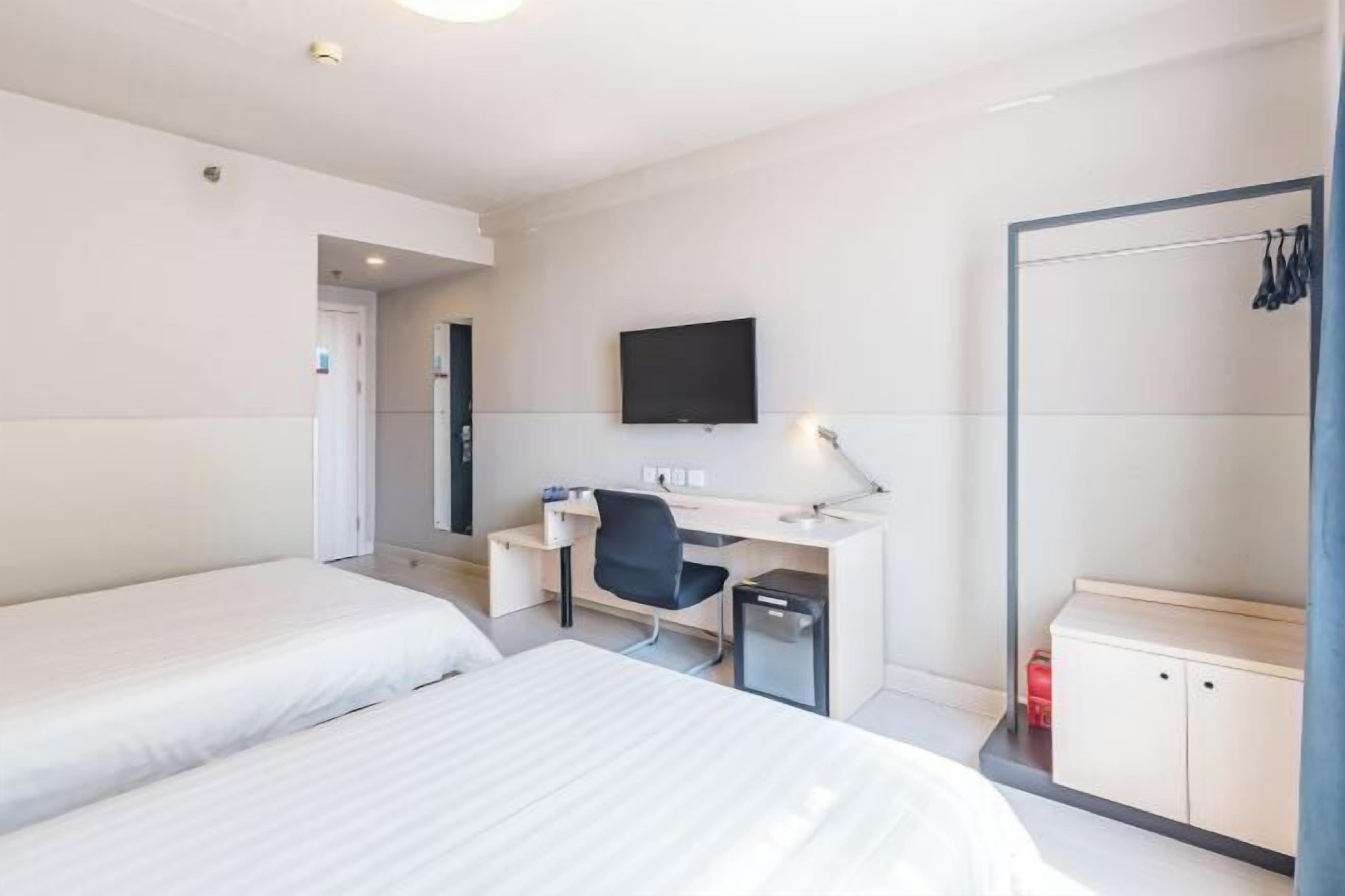 Ein Hotelzimmer mit zwei Betten, einem Schreibtisch mit Stuhl, einem Fernseher und einem Kleiderschrank.