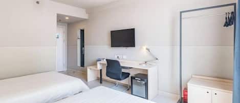 A hotel room with two beds, a desk with a chair, a TV, and a wardrobe.
