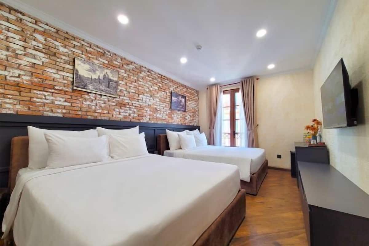 A hotel room with two beds, a brick wall, a flat-screen TV, and a window with curtains.