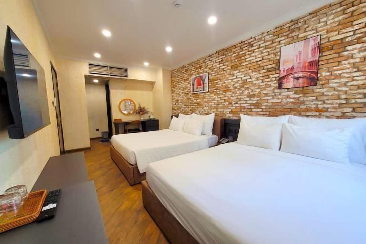 A hotel room with two beds, a TV, a desk, and a brick-patterned wall.