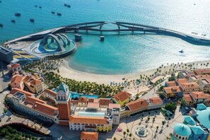 Vista aérea de una zona costera con playa, un puente y un conjunto de edificios con varios tejados y una estructura central con cúpula.