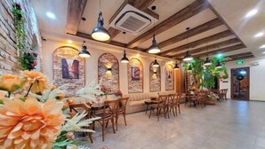 A restaurant with wooden tables and chairs, stone walls, and hanging pendant lights. - Juliet Boutique Hotel - Sunset Town (Phu Quoc Island)
