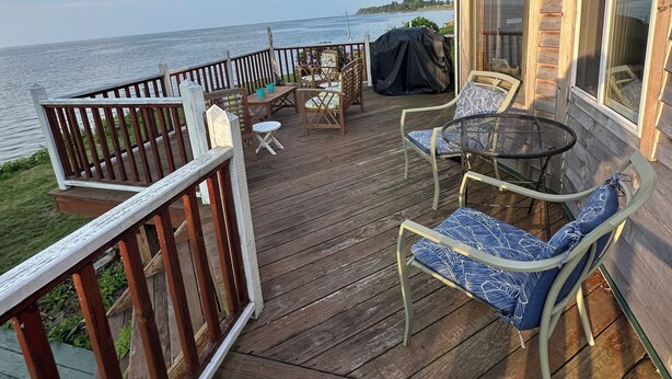 Une terrasse en bois, aménagée avec du mobilier d’extérieur, notamment des chaises et une table, et offrant une vue sur une étendue d’eau.