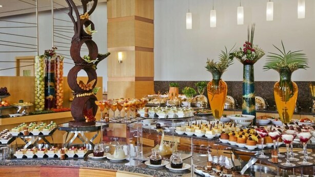 Un buffet proposant une variété de plats et de boissons, une sculpture d’arbre décorative et des vases ornés de plantes.