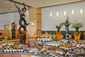 A buffet with various food items and drinks, a decorative tree sculpture, and vases with plants. - Bisila Palace (Malabo)