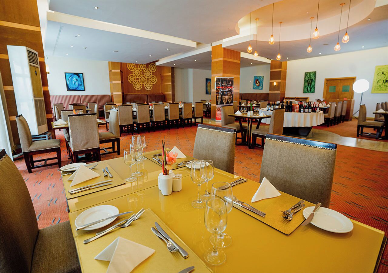 Un comedor de hotel con mesas amarillas dispuestas para comer, sillas y una zona de buffet al fondo.