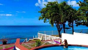 A swimming pool with a view of the ocean, surrounded by a white fence and palm trees. - Ocean front 2-bedroom house private Beach, pool in enchanting Rincon wifi AC (Rincon)