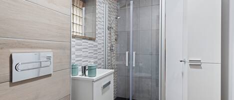 A modern bathroom with a glass shower enclosure, a white sink with a soap dispenser, and a towel rack.