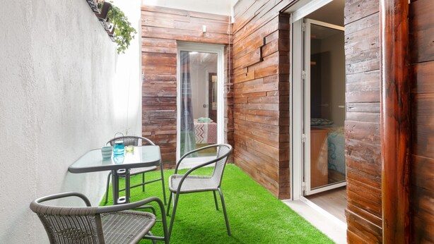 A small patio with a glass table and wicker chairs, a wooden wall, and a sliding glass door leading to an interior room. - Burriana Centro (Burriana)