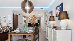 A modern dining area with a wooden table set for four, a chandelier, and a white cabinet with a glass display. - Burriana Centro (Burriana)