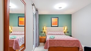 A hotel room with two beds, a mirror, a nightstand, and a wall-mounted lamp. - Burriana Centro (Burriana)