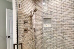 Un bagno con parete in mattoni, cabina doccia in vetro e un piccolo ripiano con articoli da toilette.