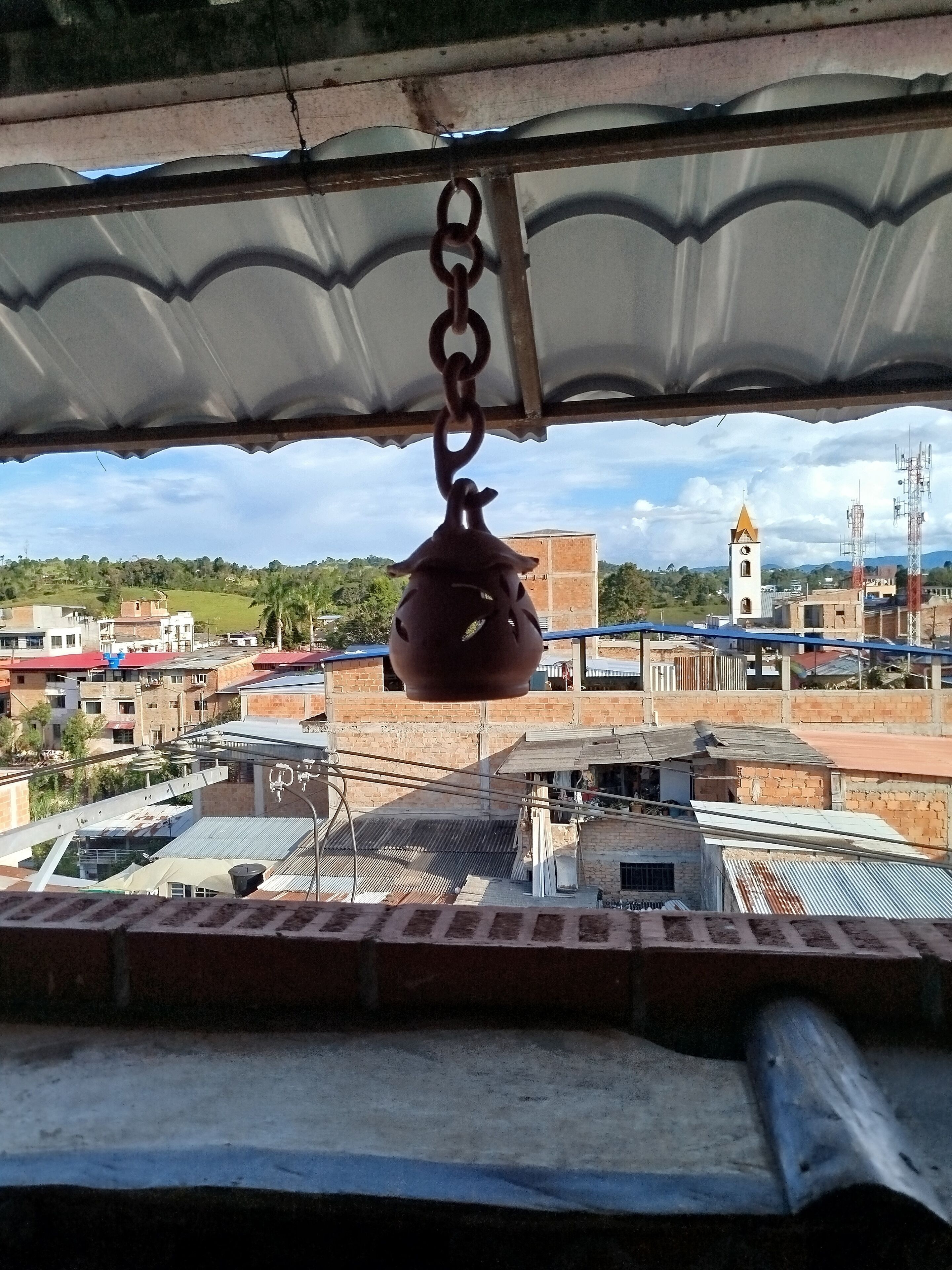 Uma panela pendurada sob um telhado, com vista para prédios e uma torre ao fundo.