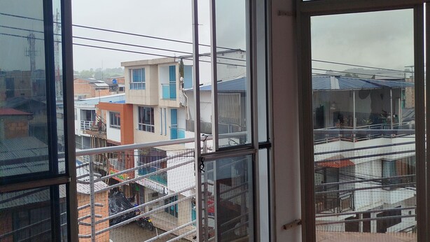 A room with large sliding glass doors leading to a balcony with a view of buildings and a fence. - Hotel Ancestral Rojas coffee (San José de Isnos)