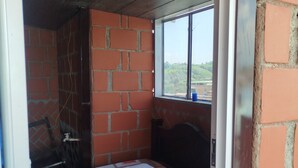 A small, single-bed room with a brick wall and a window. - Hotel Ancestral Rojas coffee (San José de Isnos)