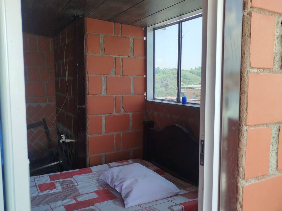 Una habitación pequeña con cama individual, pared de ladrillo y ventana.