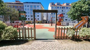 A playground with a wooden fence, colorful play area, and buildings in the background.