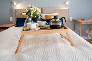 A neatly made bed with a wooden tray holding a coffee pot, cups, and a vase of flowers.